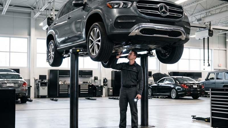 Механик осматривает днище Мерседес на подъемнике в автосервисе